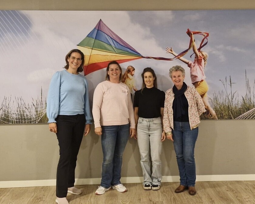 De vier therapeuten van de werkgroep Zie je mij van Gezondheidscentrum Broekpolder, lachend voor een wand met een regenboogvlieger